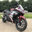 Load image into Gallery viewer, Red and white sports motorcycle parked on a paved surface with greenery in the background.